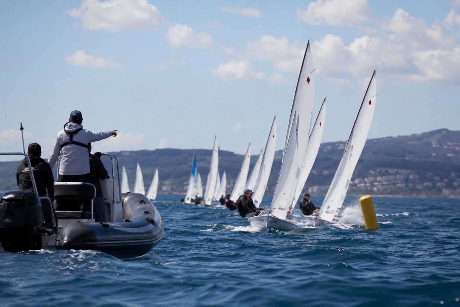 Racing dinghy fleet at a sailing event with a coach boat nearby